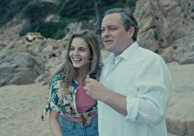 Two people standing on a beach smiling and looking out.