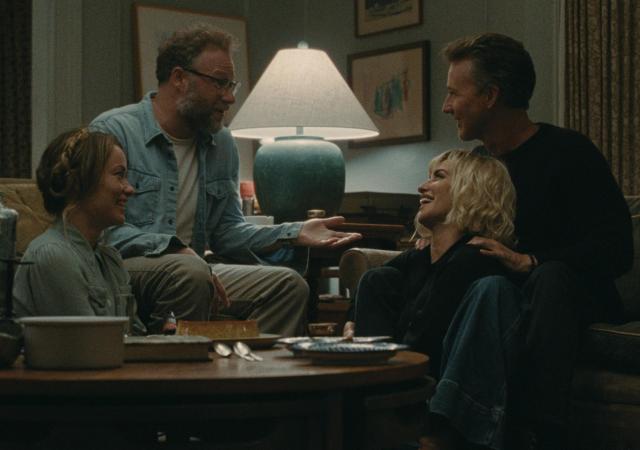 four people sit in a living room laughing and talking