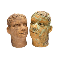 Two ceramic heads, they look aged and have a natural red clay color. The head on the right appears to have some growth on it, resembling mold or other plant life. The heads face slightly inward and are looking sightly upward. Both heads are included in Meghan Sullivan's "This Little World"