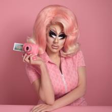 Trixie Mattel dressed in pink holding a pink Polaroid camera.