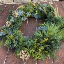 Handmade evergreen wreath sitting on a wooden table next to a pair of pliers