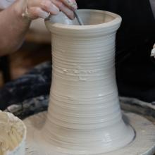 Hands working on a tall ceramic vase.