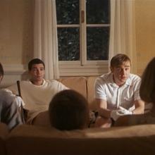 Still from film Funny Games (1997), family sits on couch and home invaders sit across from them.