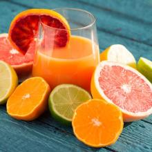 Picture of orange juice cup surrounded by slices of other citrus fruit sitting on blue table.