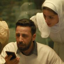 Still from film The Voice of Hind Rajab, four people stand around a phone on a call.