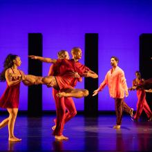 Dancers in red in a pose in front of purple background.