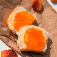 A peach jam sandwich on brown paper with slices of peaches