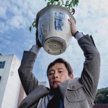Still from film No Other Choice, man holds potted plant over his head.