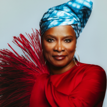 Angelique Kidjo standing in front of a light blue background.