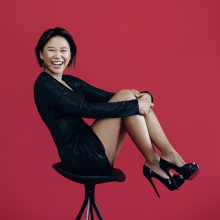 Yuja Wang sitting on a stool in front of a red backdrop.