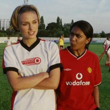 two female socker players, one with a white jersey (left) and one with a red jersey (right)