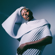 anaiis standing in front of a white and blue backdrop.