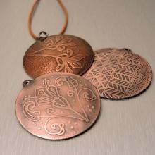 Photo of three necklace pendants that are copper etched. 