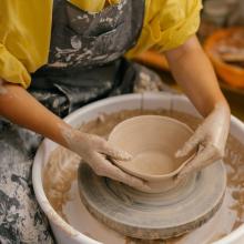 Photo of someone making a clay bowl on a pottery wheel.