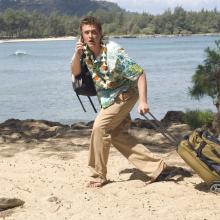 man dragging suitcase across beach with a body of water behind him