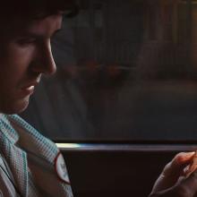man in car staring at phone with shadowed figure in doorway in background