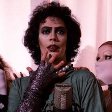 Individual in spooky makeup looks shocked, two individuals in surgical masks look at them.