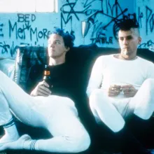 Two individuals with punk style sitting in a graffiti-filled room with beers.