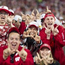 A group of UW–Madison fans cheering at the sidelines of a football game.