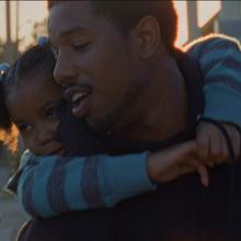 Father dressed in black giving his daughter wearing blue, a piggy back. Both looking frame left.