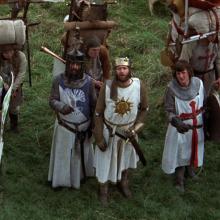 5 individuals dressed as medival knights looking up, with sheilds and swords.  