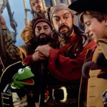 Muppets in pirate uniforms on a boat with 3 individuals also dressed as pirates.