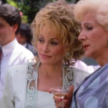 Two older women gossip at an outdoor party with pastel decor 