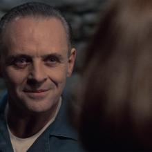 man in prison blue jumpsuit smiling creepily at a woman.