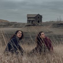 Tommy Lefroy duo sitting in a field of dried grass with a house far behind.