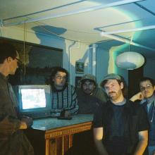 Discus band members standing around a desk with a monitor