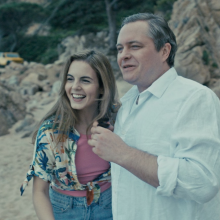 Two people standing on a beach smiling and looking out.